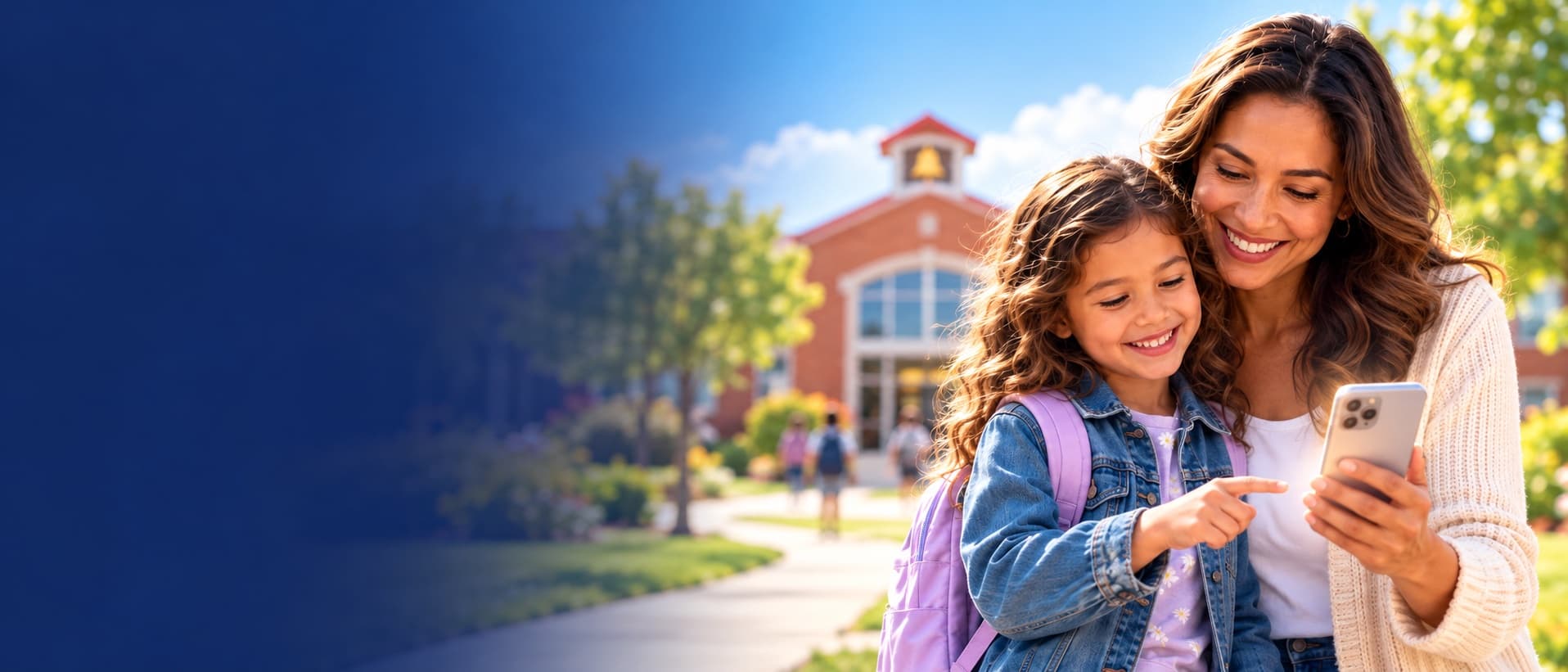 A mother and her daughter smiling at a phone together outside an elementary school at the end of the day.